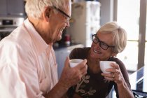 Старшая пара улыбается, когда пьет кофе дома на кухне — стоковое фото