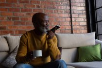 Seniorchef trinkt Kaffee, während er daheim mit dem Handy telefoniert — Stockfoto