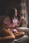 Mujer tomando café frío mientras usa el teléfono móvil en casa - foto de stock