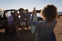 Amiga clicando fotos de amigos com telefone celular na praia — Fotografia de Stock