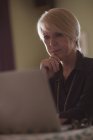 Задумчивая зрелая женщина использует ноутбук дома — стоковое фото