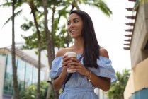 Улыбающаяся красивая женщина держит чашку кофе на улице — стоковое фото