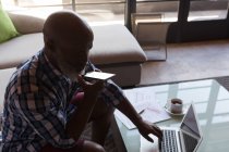 Пожилой мужчина пользуется ноутбуком, разговаривая дома по мобильному телефону — стоковое фото