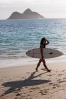 Femme marchant avec planche de surf à la plage par une journée ensoleillée — Photo de stock