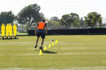 Jogador de futebol driblando através de cones no campo esportivo — Fotografia de Stock