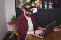 Чоловічий виконавчий за допомогою віртуальної реальності гарнітура з ноутбук на столі в офісі — стокове фото