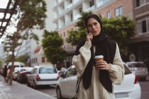 Hijab woman talking on mobile phone while having coffee at sidewalk — Stock Photo