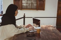 Hijab mujer usando el ordenador portátil en la mesa en la cafetería - foto de stock