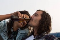 Donna che dà birra all'uomo in spiaggia al crepuscolo — Foto stock