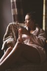Задумчивая женщина пьет кофе в гостиной дома — стоковое фото