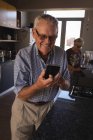 Homme âgé utilisant un téléphone portable dans la cuisine à la maison — Photo de stock