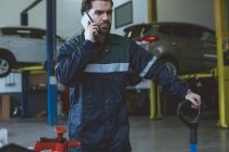 Mécanicien parlant sur un téléphone portable au garage de réparation — Photo de stock
