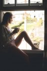 Mujer pensativa tomando café cerca de la ventana en casa - foto de stock