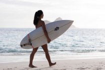 Жінка, що йде з дошкою для серфінгу на пляжі в сонячний день — стокове фото