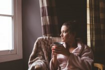 Mulher atenciosa tomando café na sala de estar em casa — Fotografia de Stock