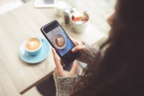 Donna cliccando foto di caffè con cellulare in caffetteria — Foto stock