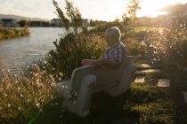 Uomo anziano rilassante sulla panchina vicino al lungofiume in una giornata di sole — Foto stock
