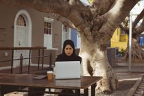 Красива міська хіджаб жінка використовує ноутбук у тротуарному кафе — стокове фото
