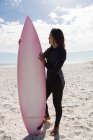 Жіночий серфер стоїть з дошкою для серфінгу на пляжі в сонячний день — стокове фото