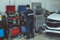 Mecánico usando el ordenador portátil mientras se repara el coche en el garaje - foto de stock