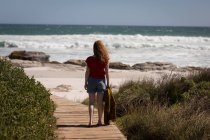 Vue arrière de la femme debout sur une planche de bois à la plage — Photo de stock