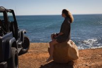 Задумчивая женщина сидит на камне на пляже — стоковое фото