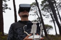 Hombre operando un dron volador mientras usa auriculares de realidad virtual en el campo - foto de stock