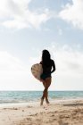 Femme courant avec planche de surf sur la plage par une journée ensoleillée — Photo de stock