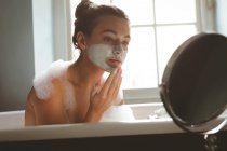 Woman applying moisturizer cream while taking bath in bathroom at home — Stock Photo