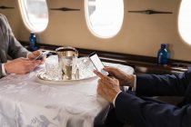 Средняя часть бизнес-людей, использующих мобильный телефон в частном самолете — стоковое фото