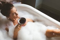 Femme ayant café noir tout en prenant un bain moussant dans la salle de bain — Photo de stock