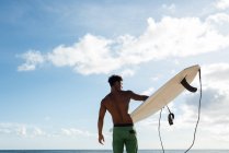 Rear view of male surfer walking with surfboard in the beach — Stock Photo