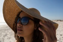 Mulher atenciosa de chapéu em pé na praia — Fotografia de Stock