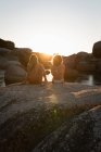 Visão traseira do casal sentado junto em uma rocha na praia — Fotografia de Stock