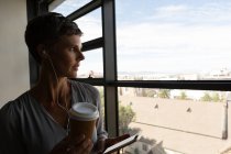 Зріла бізнес-леді слухає музику на навушниках біля вікна офісу — стокове фото