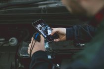 Механик фотографирует двигатель автомобиля с мобильным телефоном в ремонтном гараже — стоковое фото