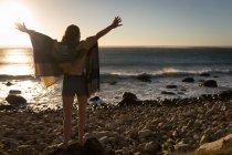 Femme avec les bras tendus debout sur le rocher au coucher du soleil — Photo de stock