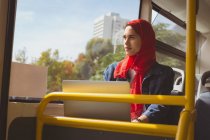Belle femme hijab avec ordinateur portable regardant par la fenêtre dans le bus — Photo de stock