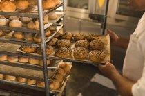 Мужской пекарь удаляет поднос со сладкими продуктами в пекарне — стоковое фото