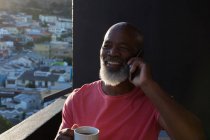 Старший чоловік має каву під час розмови на мобільному телефоні вдома — стокове фото