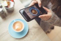 Donna cliccando foto di caffè con cellulare in caffetteria — Foto stock