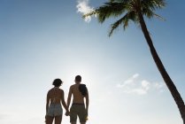 Vista posteriore di coppia in piedi con mano nella mano in spiaggia — Foto stock