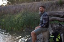 Вид збоку чоловіка, що розслабляється на пеньку біля берега річки — стокове фото