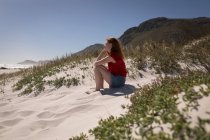 Vue latérale de la femme assise sur le sable à la plage par une journée ensoleillée — Photo de stock