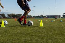Soccer player dribbling the ball through cones in sports field — Stock Photo