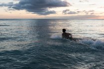 Surfista masculino surfando com prancha de surf no mar ao entardecer — Fotografia de Stock