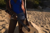 Sección media de la mujer sosteniendo la guitarra en la playa - foto de stock