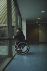 Seitenansicht eines behinderten Mannes im Rollstuhl, der aus einer Glasscheibe blickt — Stockfoto