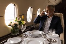 Senior businessman talking on mobile phone in private jet — Stock Photo