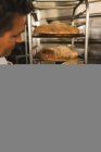 Panadero masculino revisando pan horneado en panadería - foto de stock